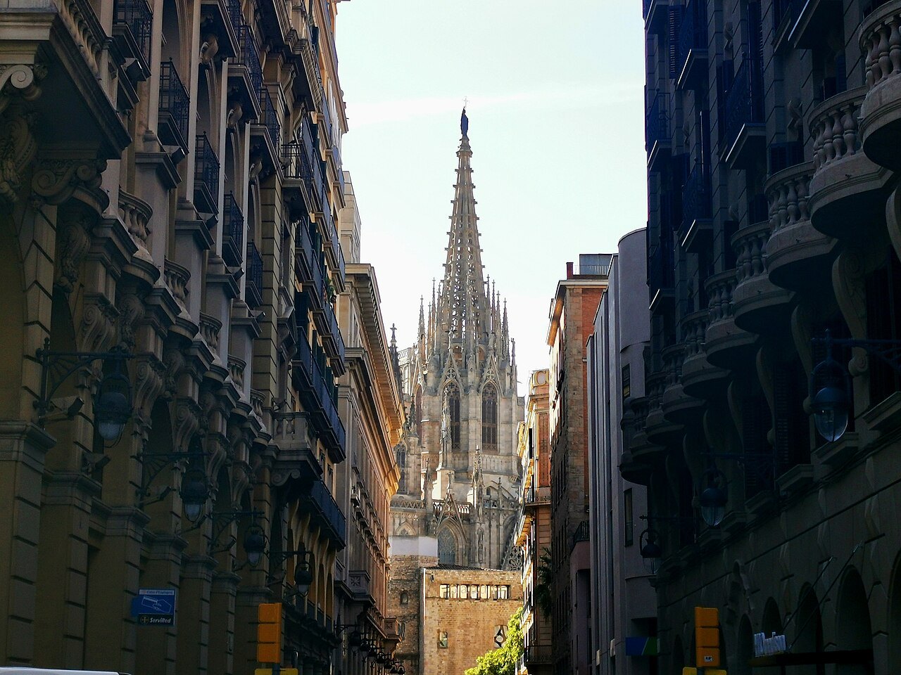 The spire of the cathedral at the end of a narrow street between tall buildings.