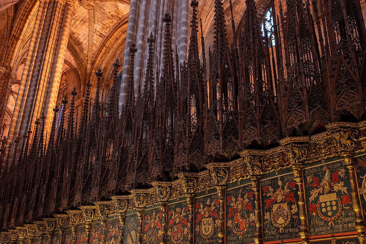Pinnacled canopies above the choir stalls, with painted coats of arms on the stall backs.