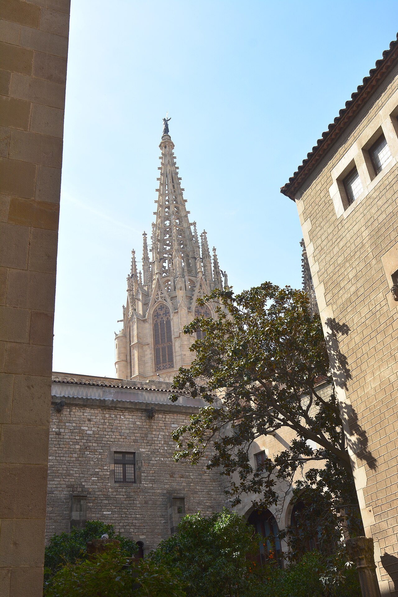 The cathedral spire rising above a courtyard wall and a tree.