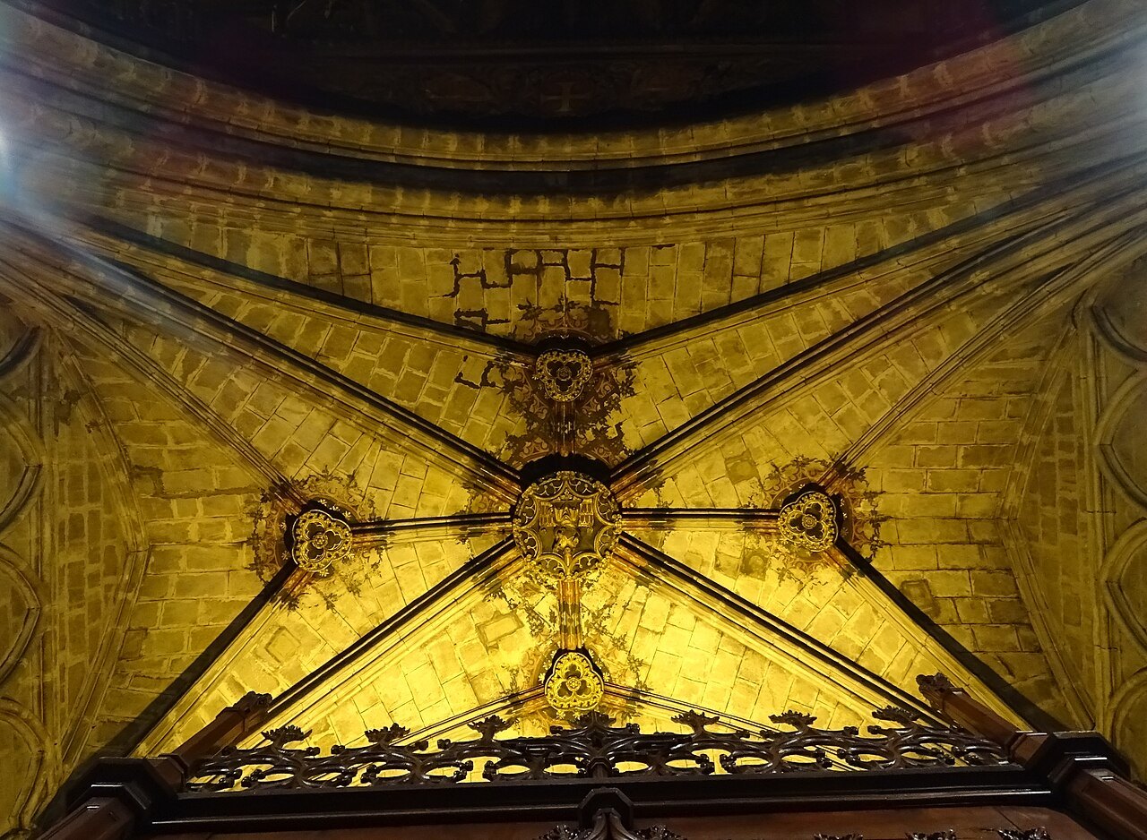 A ribbed Gothic vault lit in gold inside Barcelona Cathedral.