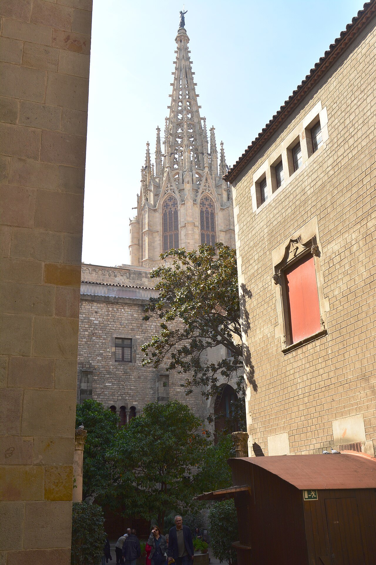 The cathedral spire seen past a stone wall and a leafy courtyard.
