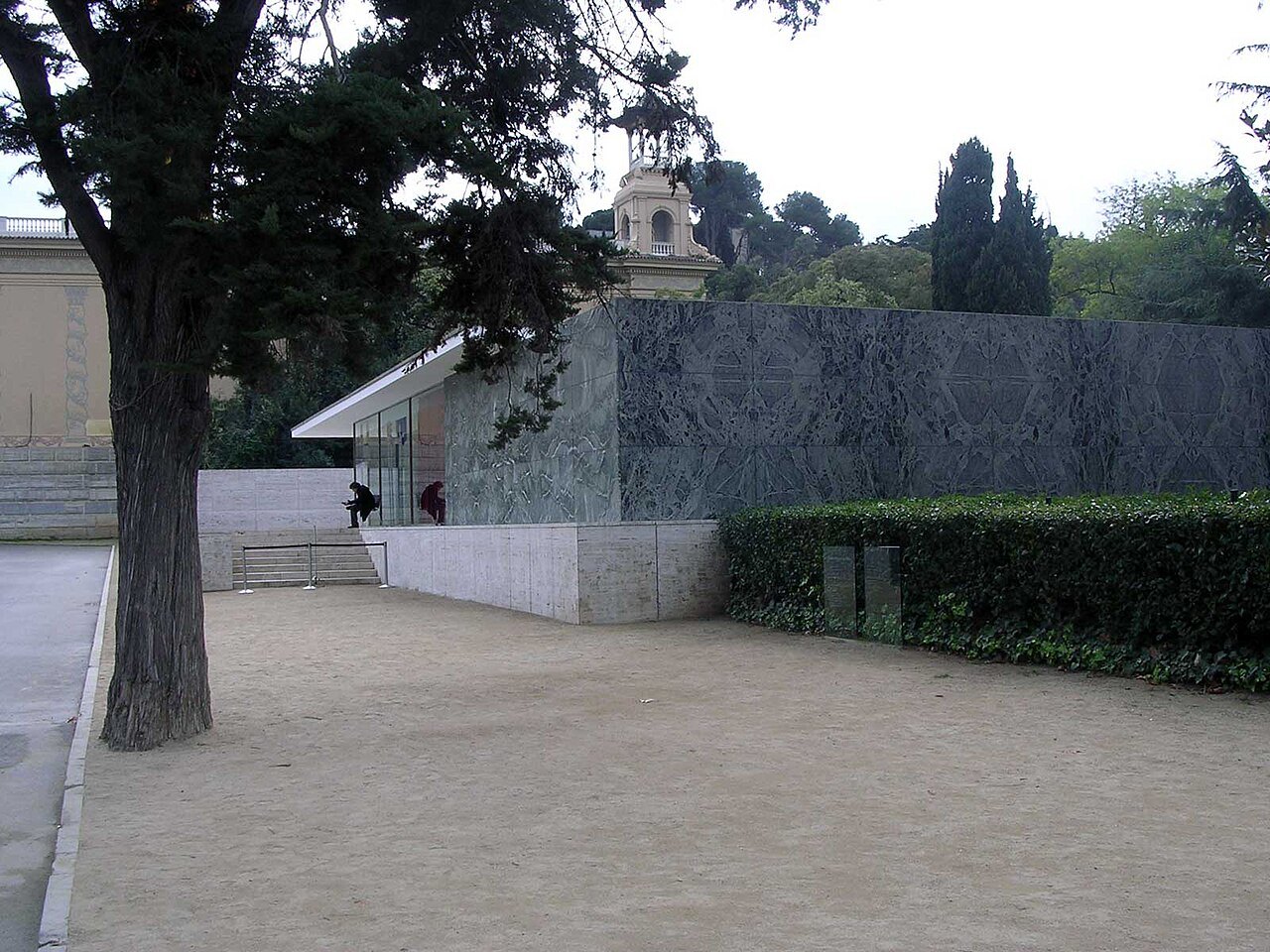 The marble wall of the pavilion seen over a hedge from the forecourt.