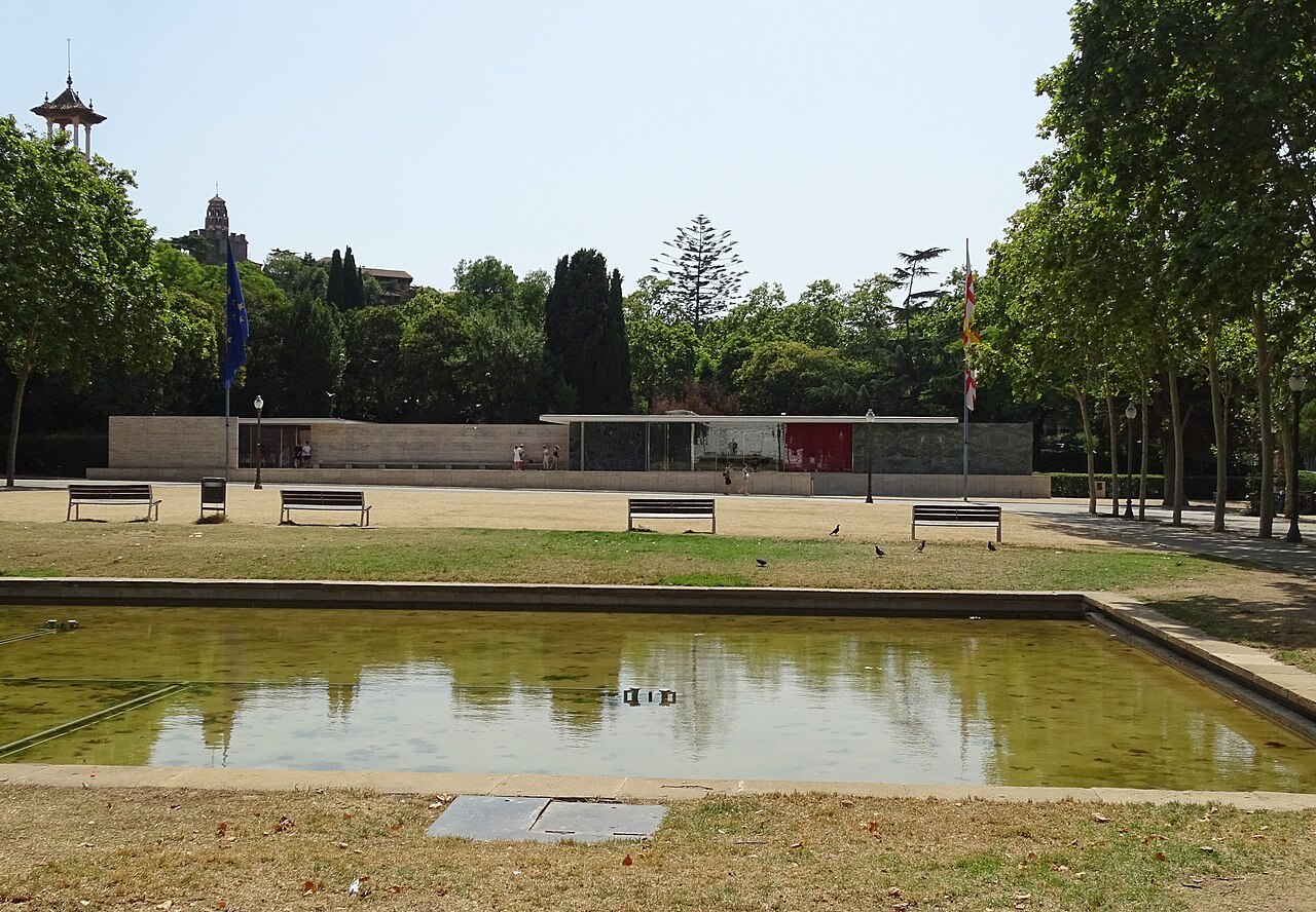 The Barcelona Pavilion low across its pool, with trees behind.