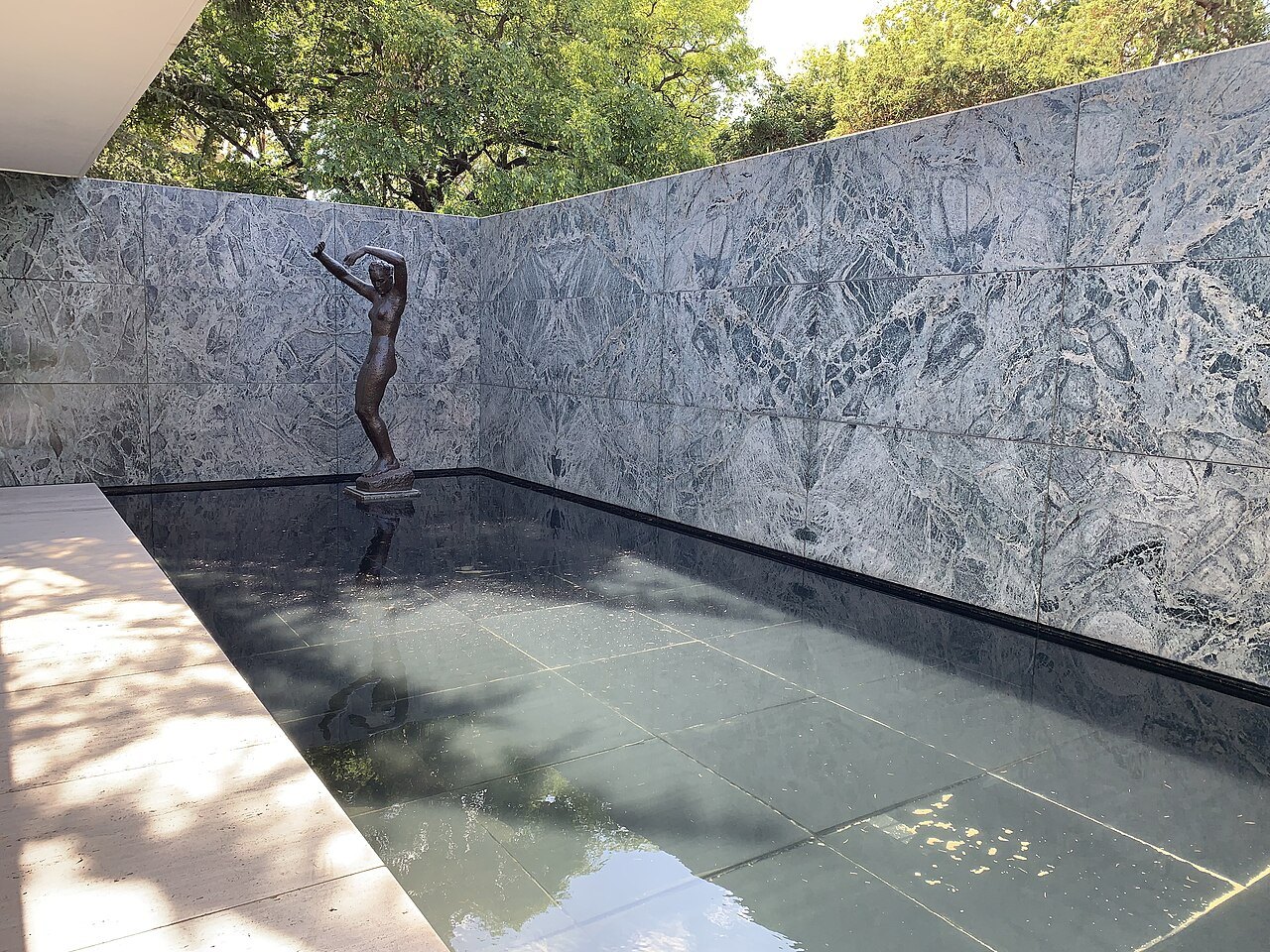 The small pool in the corner of the marble wall, with the bronze figure standing at its edge.