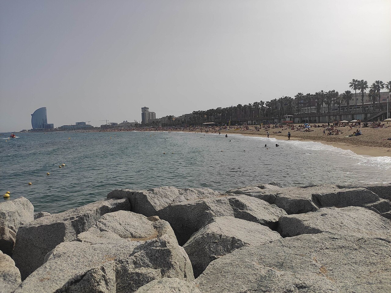 Rocks on the sand at Barceloneta beach, with the hotel tower in the haze beyond.