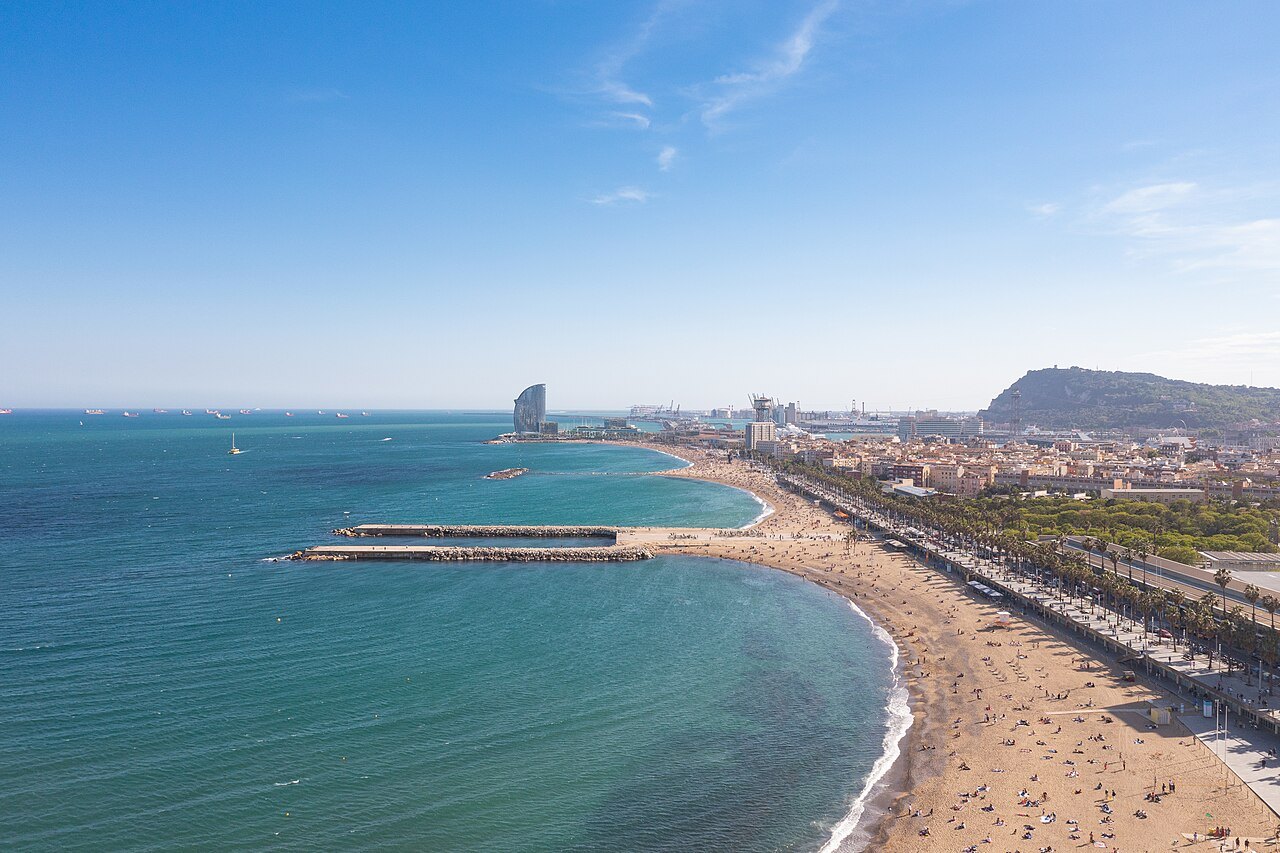 The beach and promenade curving away toward a hill, seen from the air.
