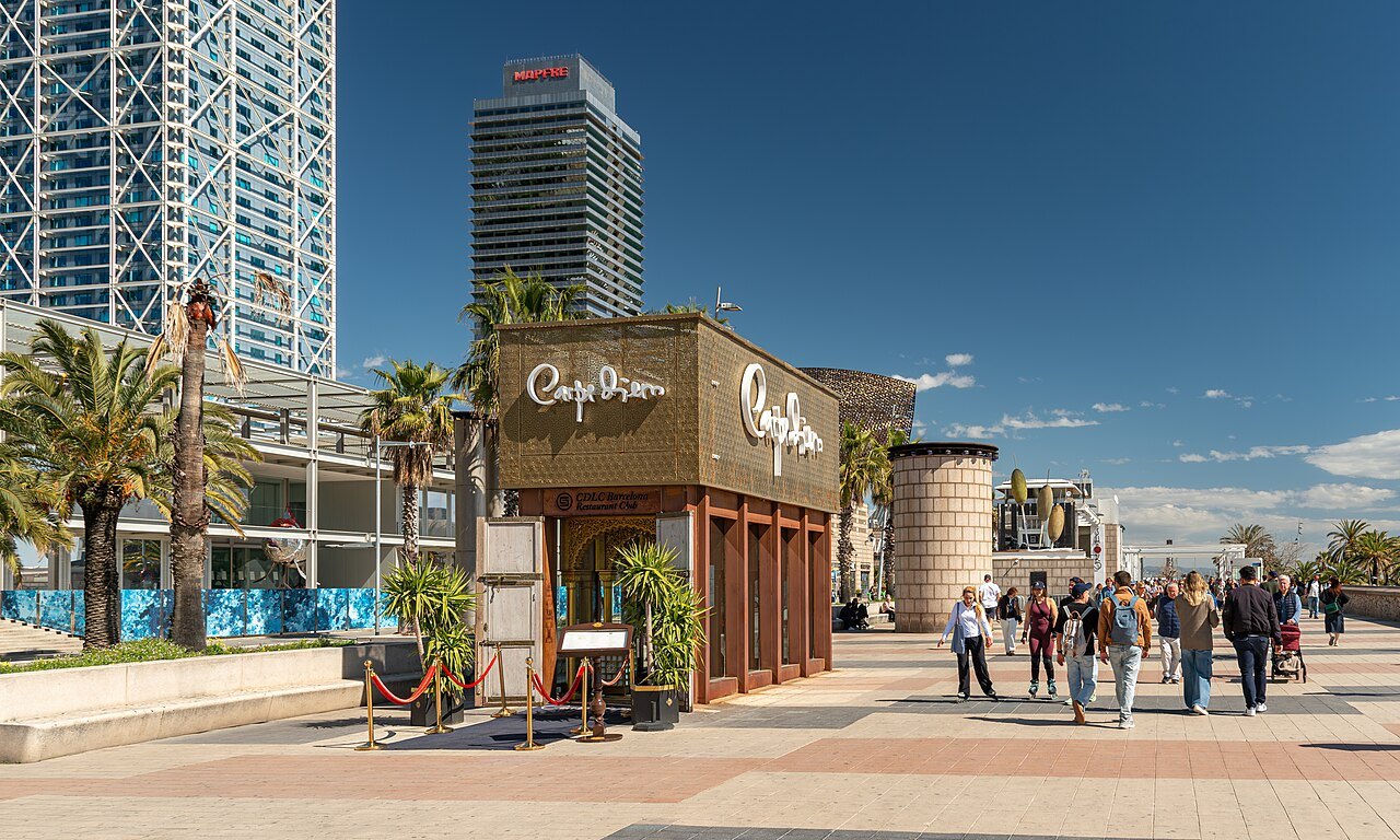 The Passeig Marítim promenade at Barceloneta, with a café pavilion and two towers behind it.