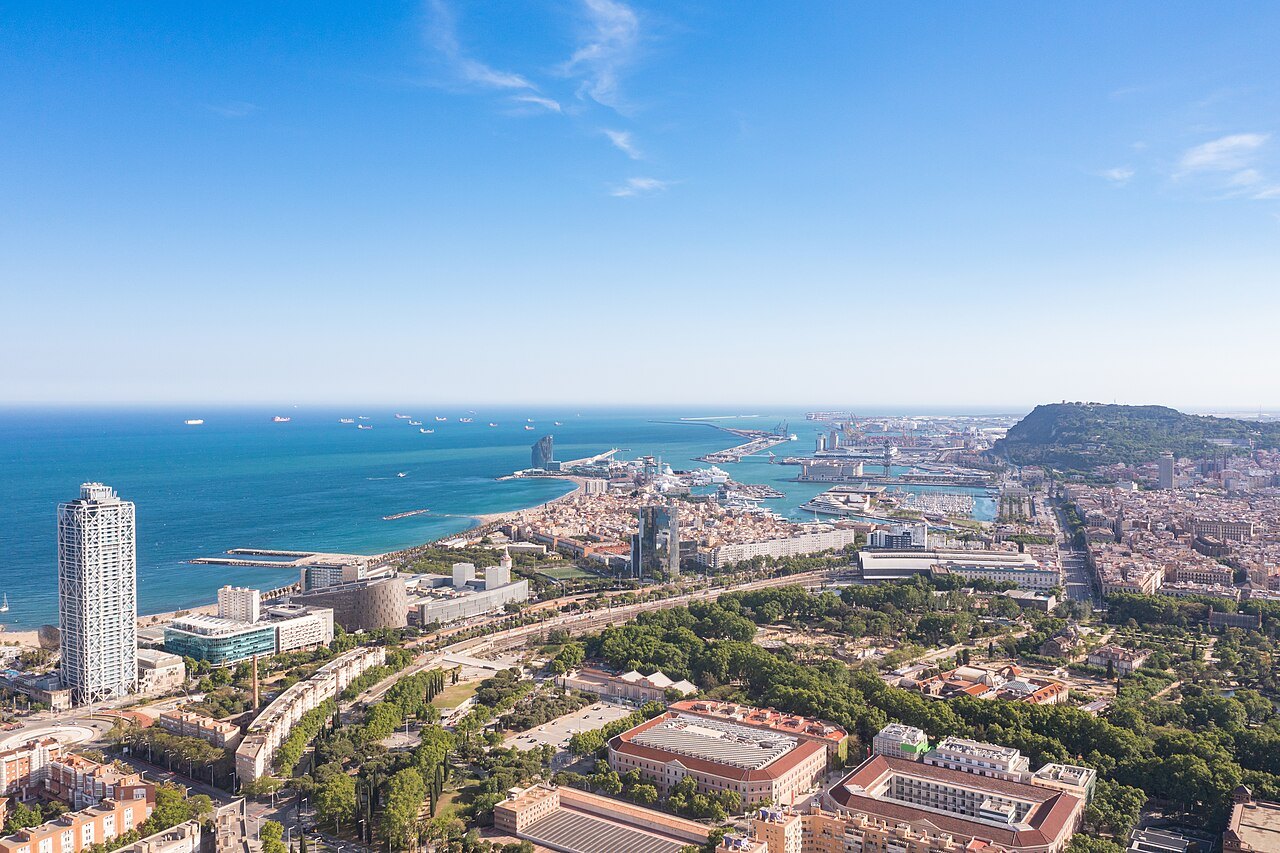 The harbor and the coast of Barcelona from above, with Montjuïc in the distance.