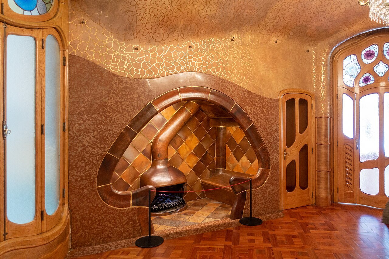 A fireplace nook with a copper hood in a warm, wood-paneled room at Casa Batlló.