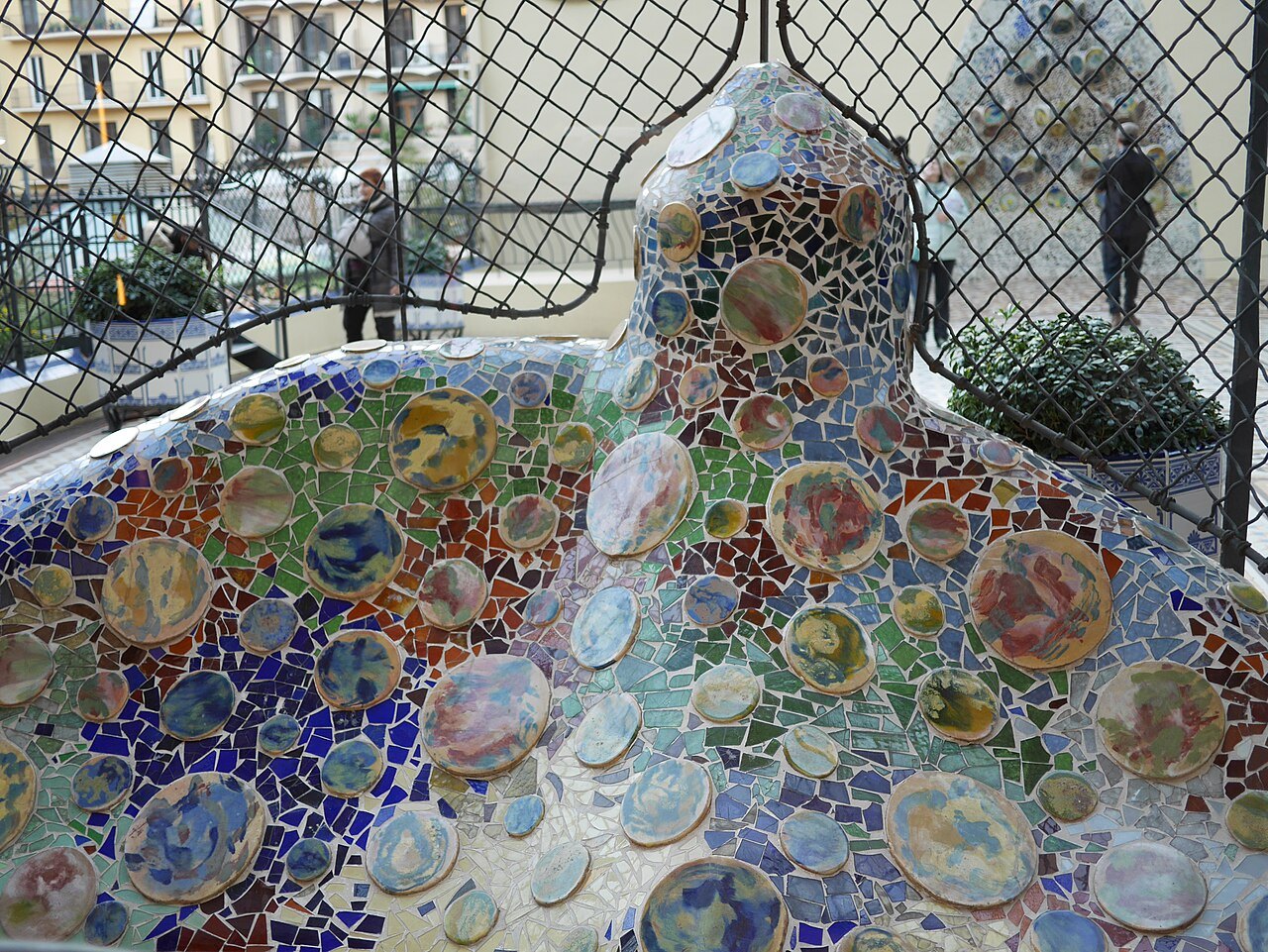 The broken-tile mosaic of the serpent bench at Park Güell, seen through the terrace fence.