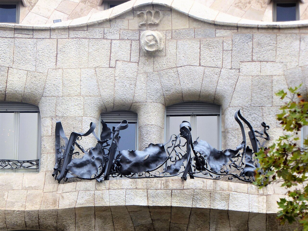 Twisting wrought-iron balcony rails on a stone façade, below a carved monogram.