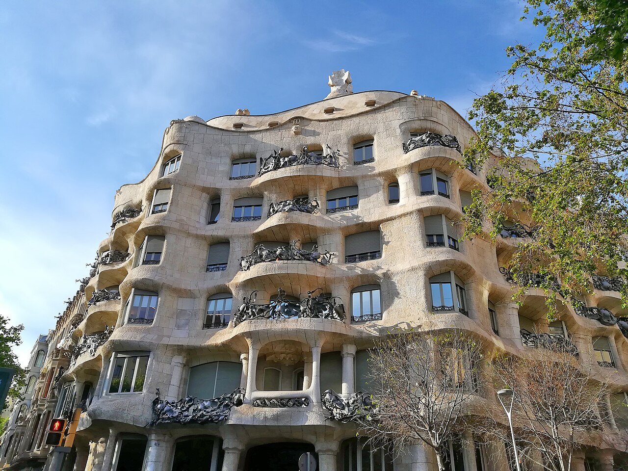 The wave-like stone façade of Casa Milà, with its twisting iron balconies and trees along the street.