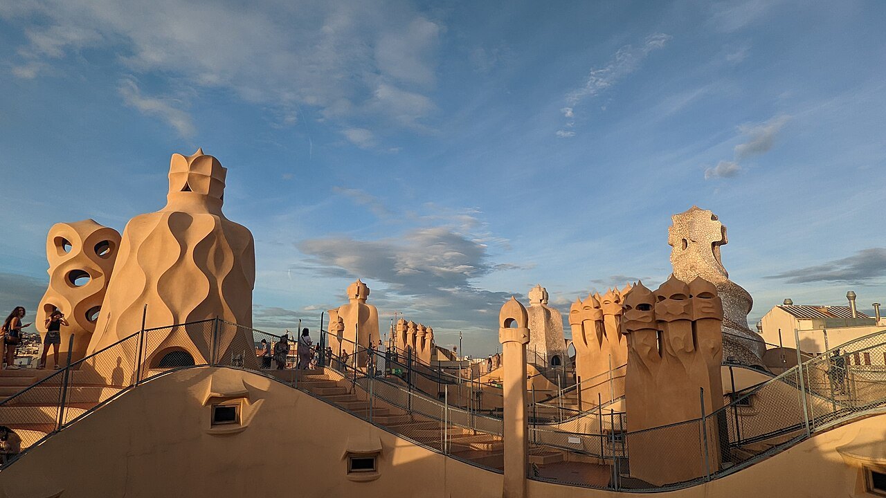 The chimneys of Casa Milà's roof terrace in the low evening light, with visitors walking among them.