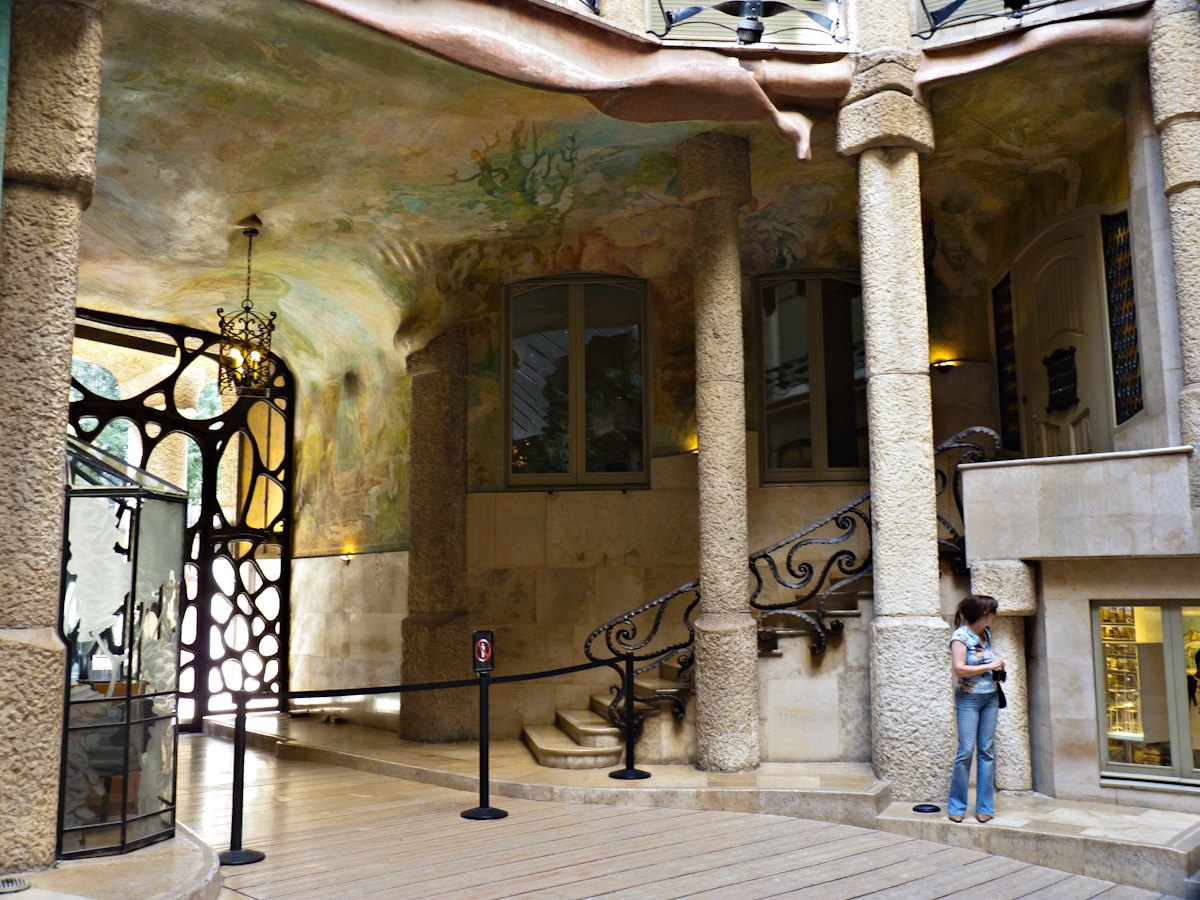 The entrance courtyard of Casa Milà, with slender columns, a painted vault and an ironwork gate.