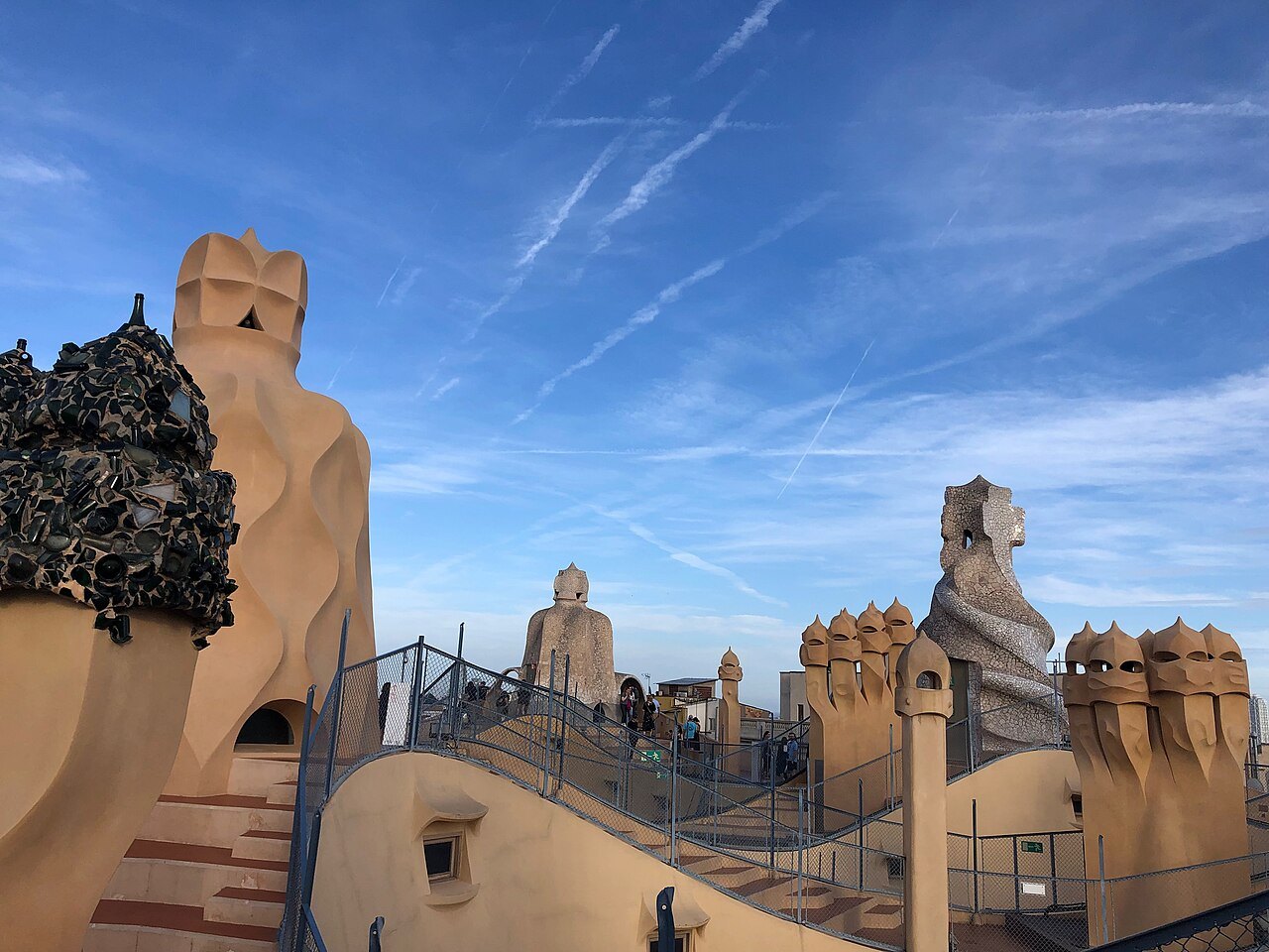 Stairs and chimneys on Casa Milà's roof against a sky streaked with contrails.