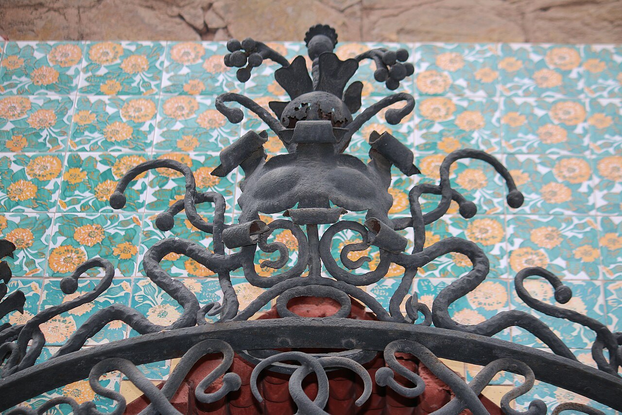 A crest of wrought iron over a wall of flower-patterned tile at Casa Vicens.