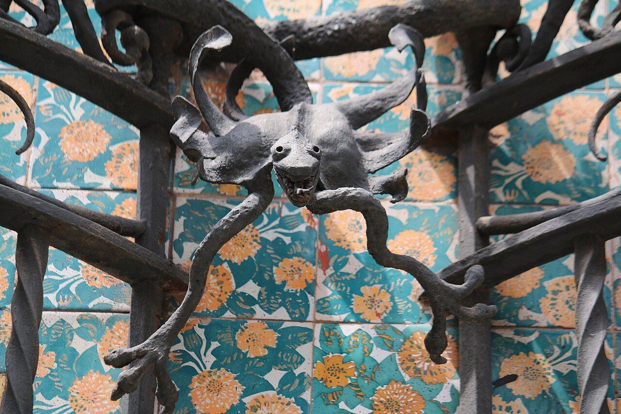 A small ironwork creature set into the gate against the marigold tiles of Casa Vicens.
