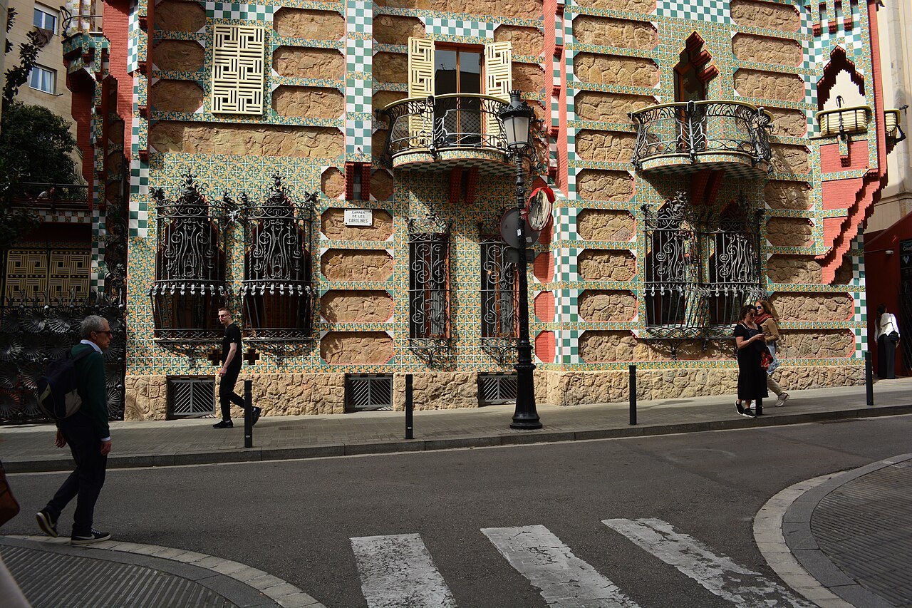 The street front of Casa Vicens from the corner, with passers-by on the sidewalk.
