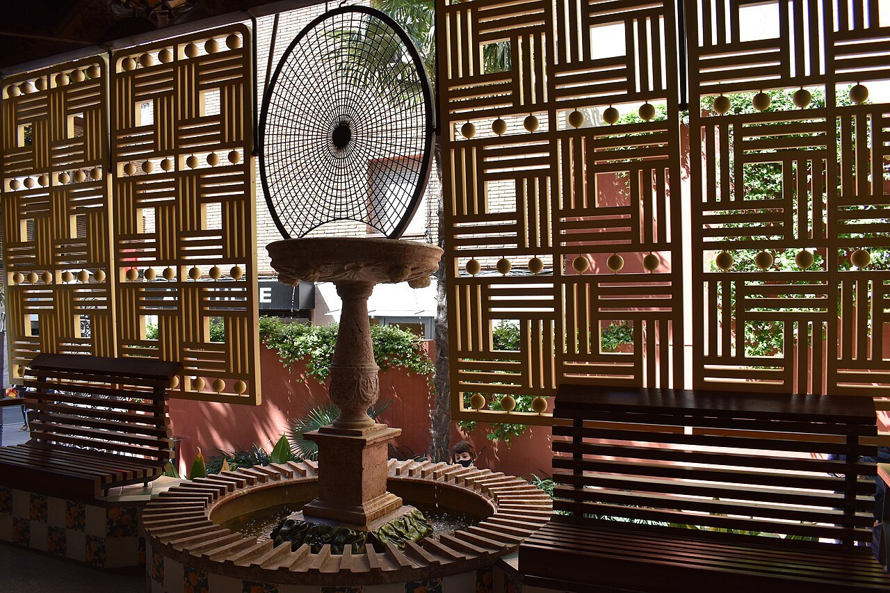 A small fountain on the porch of Casa Vicens, seen through a wooden lattice screen.