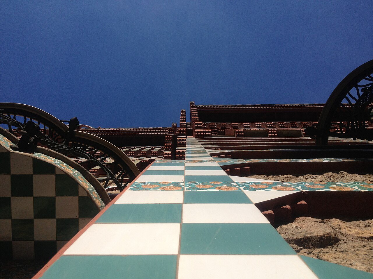 A walkway of green-and-white checkered tile on the roof of Casa Vicens, under a deep blue sky.