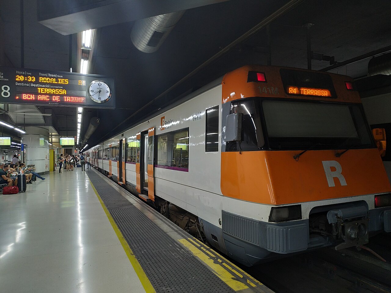 An orange-and-white Rodalies commuter train at a platform at Sants.