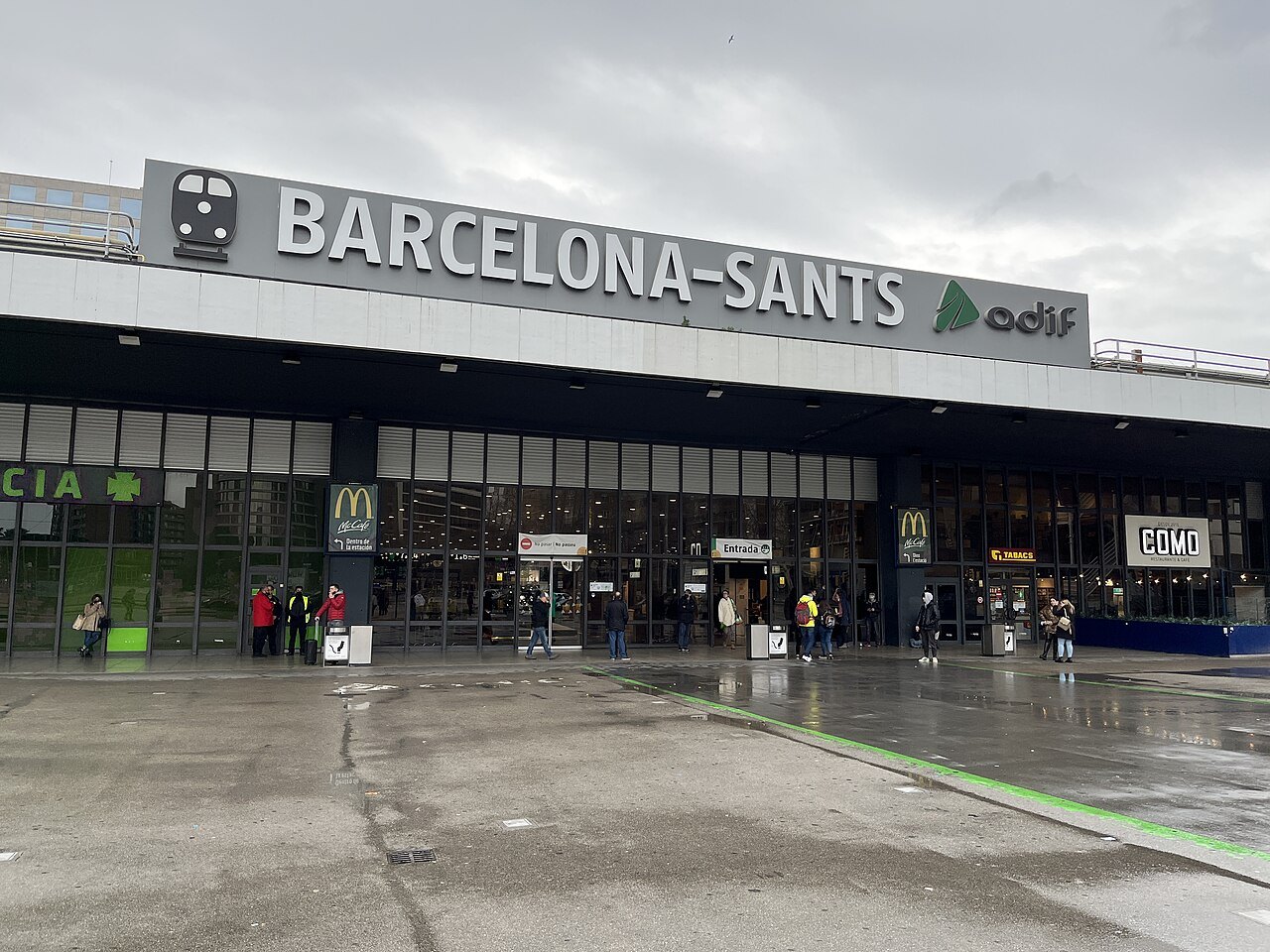 The entrance front of Barcelona Sants under its name sign, on a wet day.