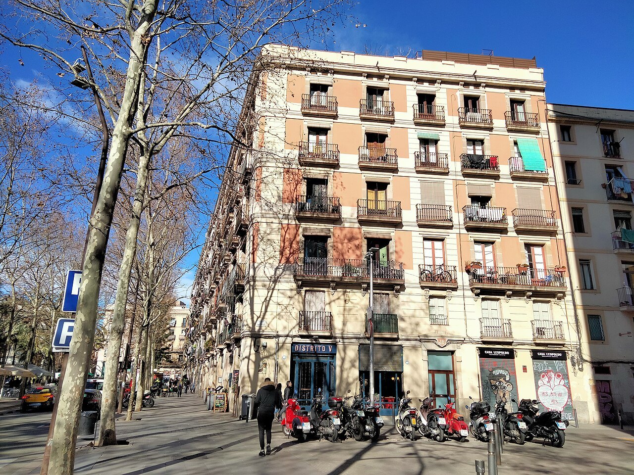 An apartment building with balconies and bare trees on a street in the Raval.