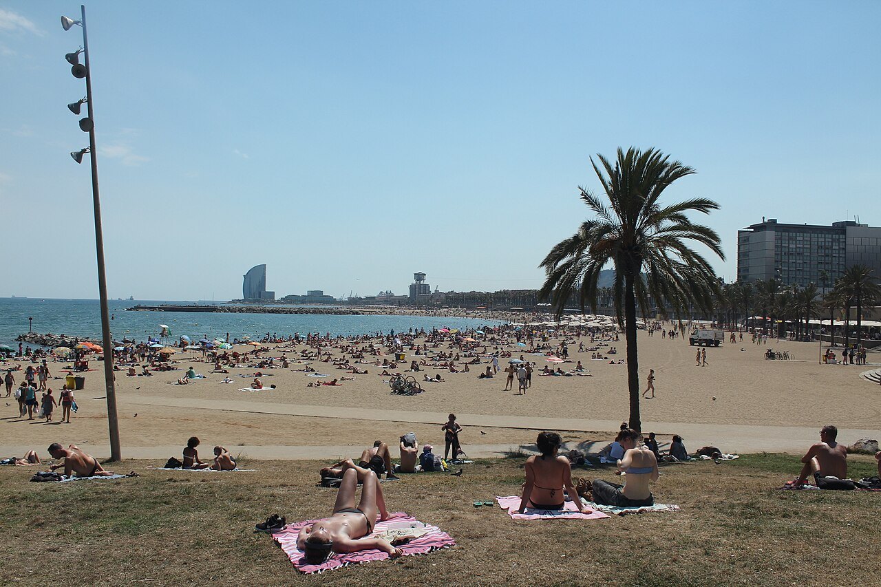 Sunbathers on the sand at the Somorrostro beach, with a hotel tower in the distance.