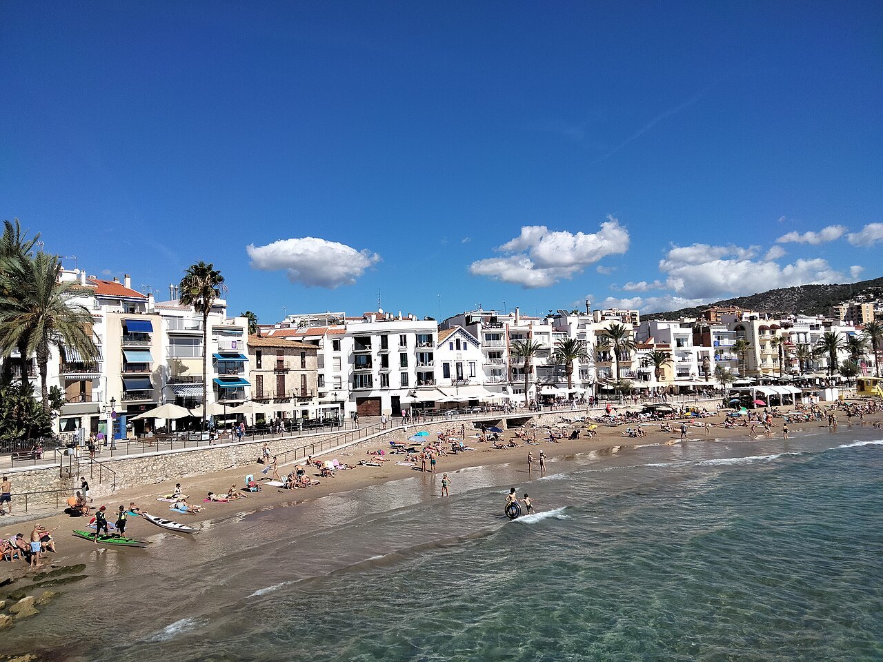 The seafront of Sitges, a line of white buildings above a sandy beach.