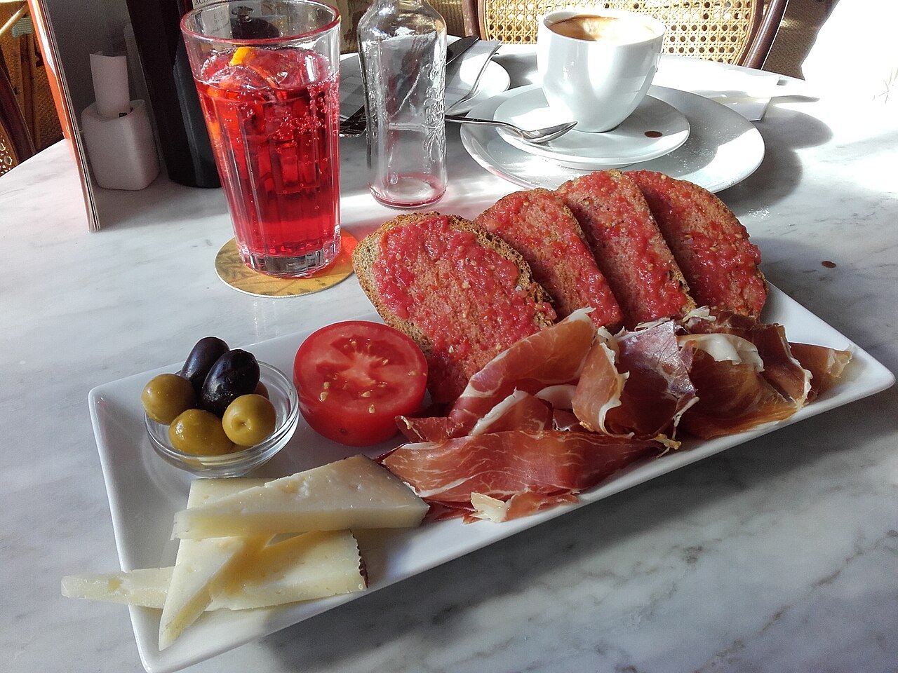 Bread rubbed with tomato, served with cured ham, cheese, olives and a glass of vermouth.
