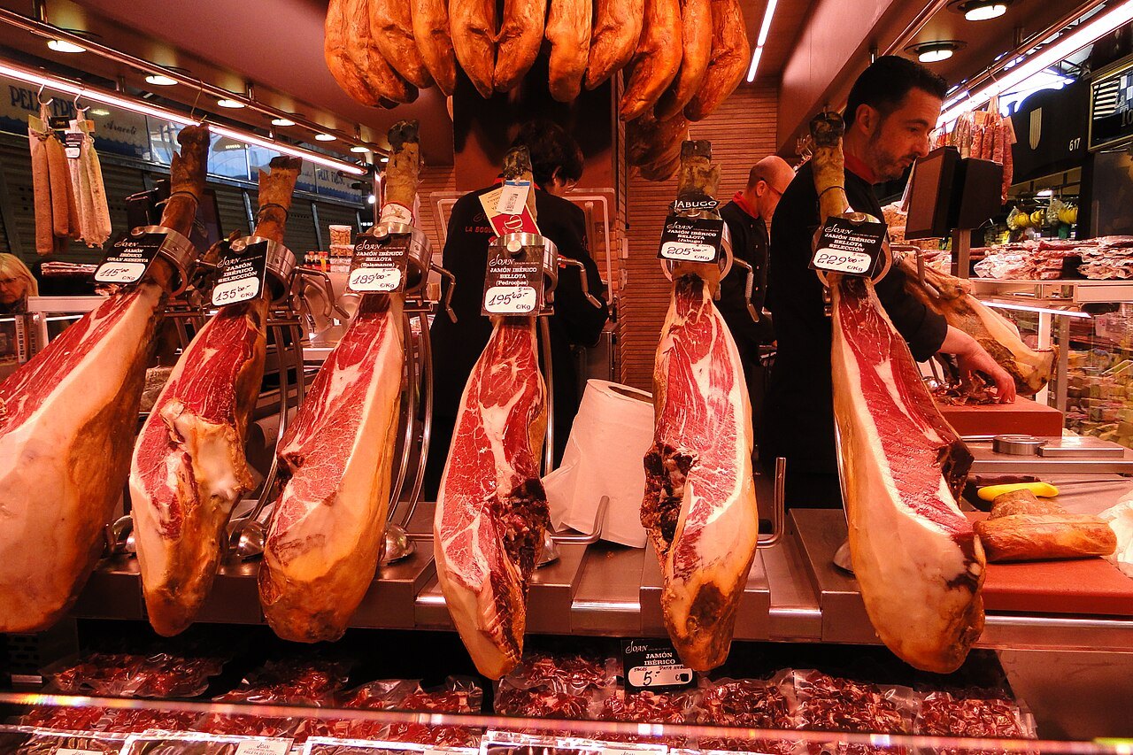 Hams hanging in a row at a market stall in the Boqueria.