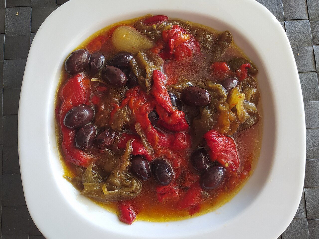 A white dish of roasted red peppers and black olives, in the manner of escalivada.