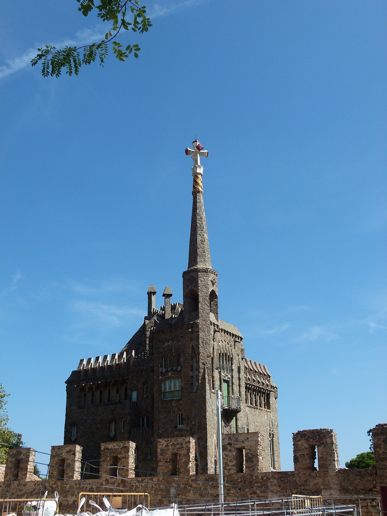 The castle-like tower of Bellesguard, topped with a cross, over a crenellated wall.
