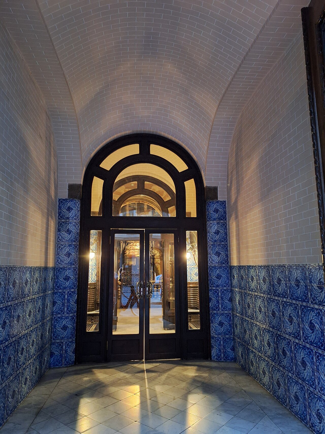 A vestibule lined in blue tile, with an arched glazed door at the end.