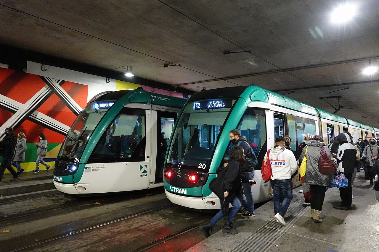Two green trams at a station platform, with passengers stepping on board.