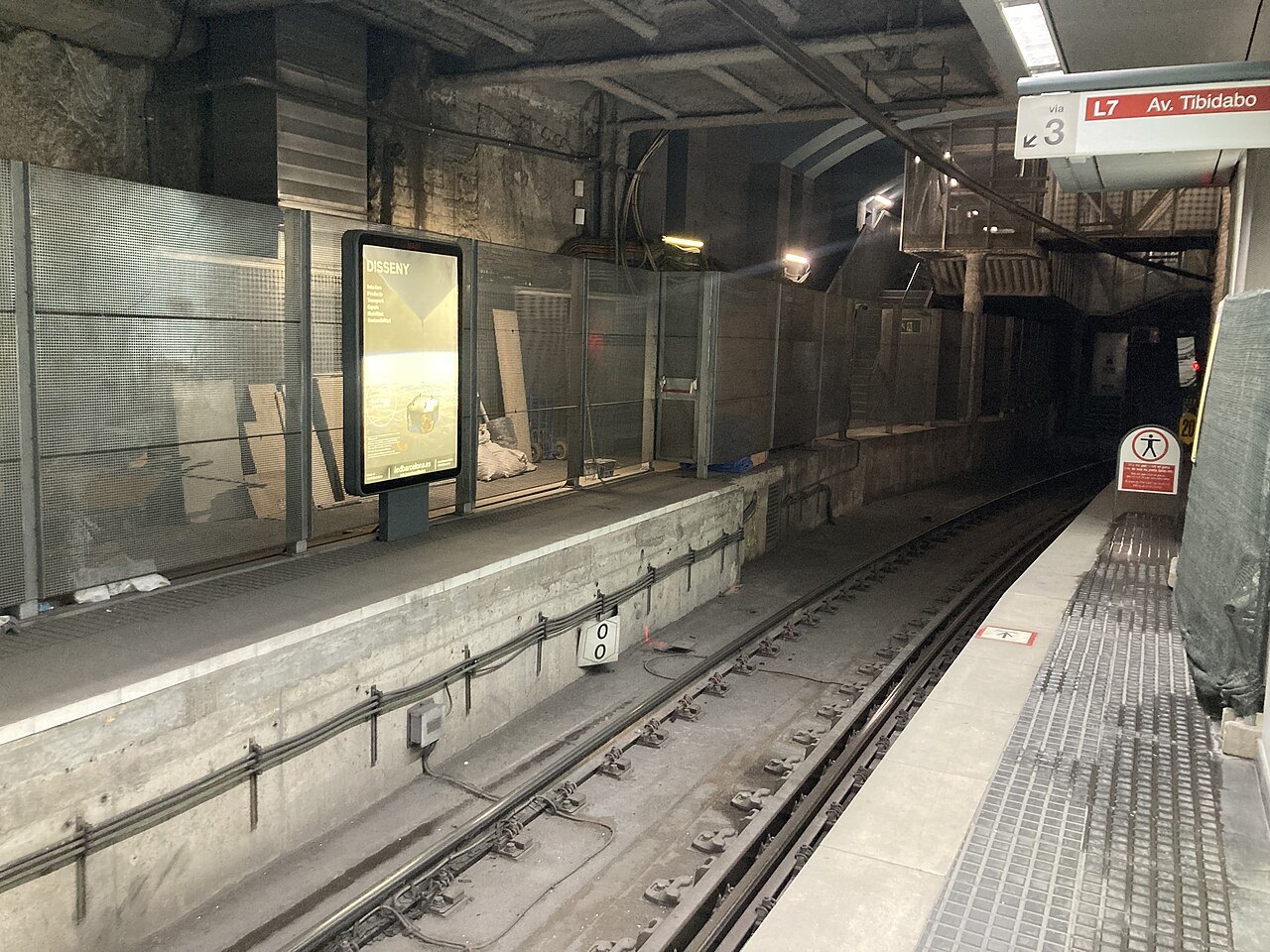 A platform with advertising screens and a tunnel mouth at Gràcia station.