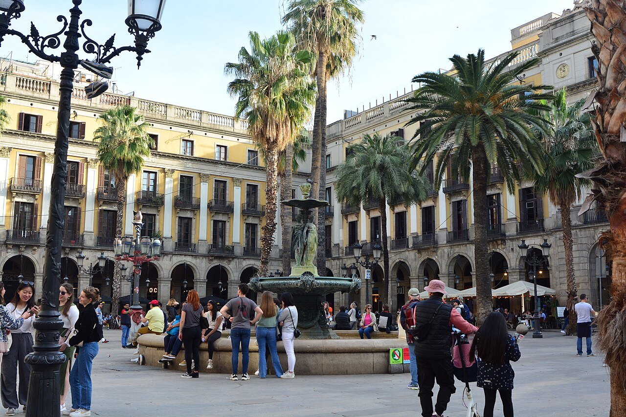 The fountain and palm trees of the Plaça Reial, with people gathered in the square.