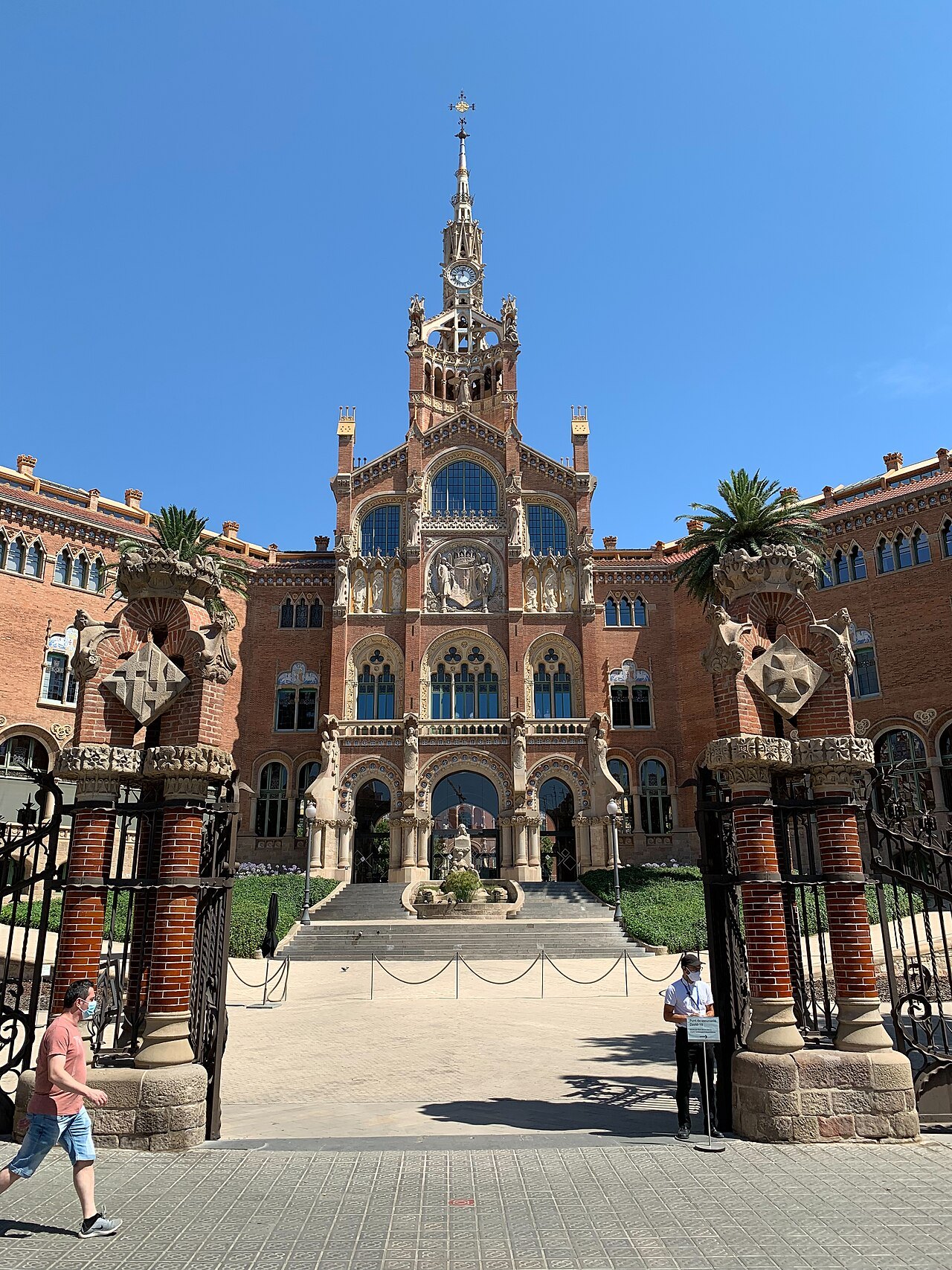 The administration pavilion of Sant Pau seen through iron gates, at the top of a flight of steps.