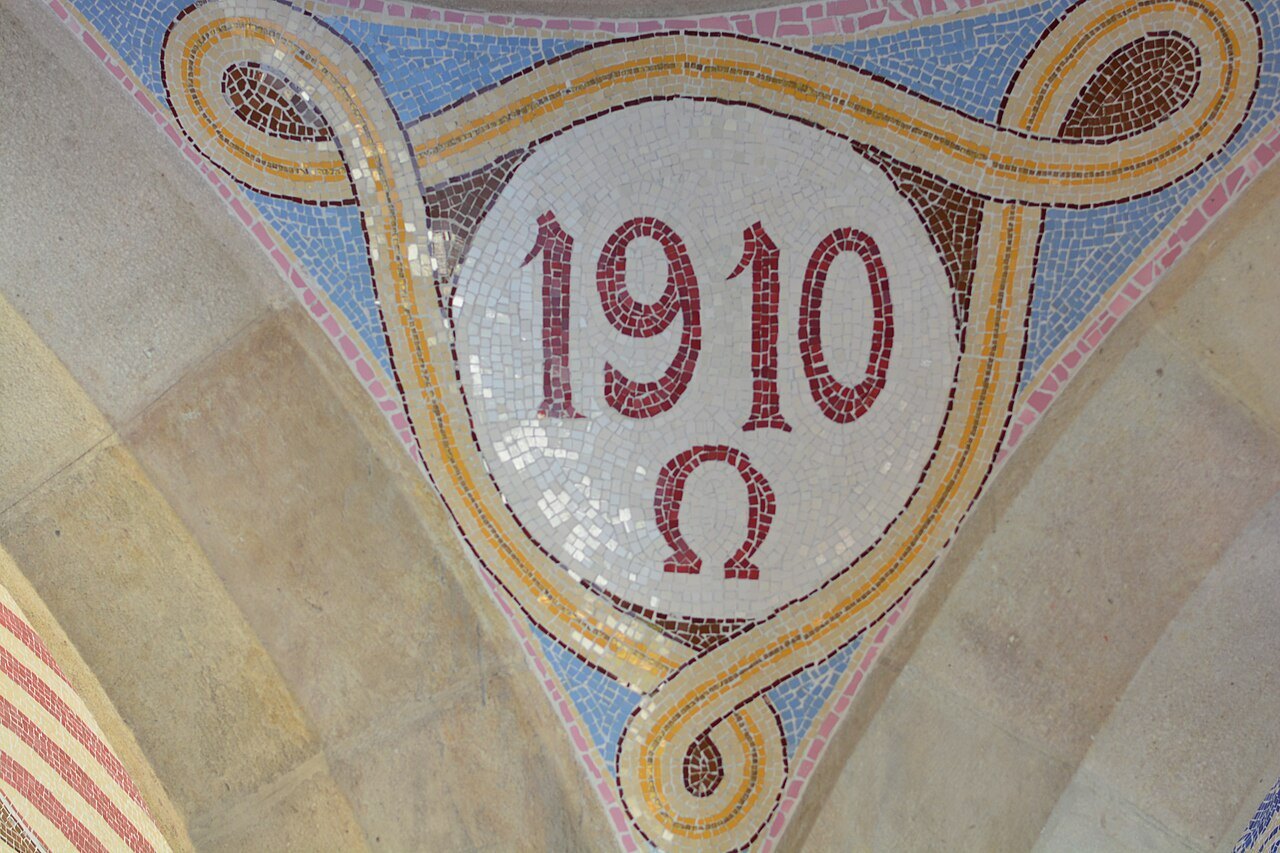 A tile mosaic medallion with the date 1910 and the Greek letter omega.