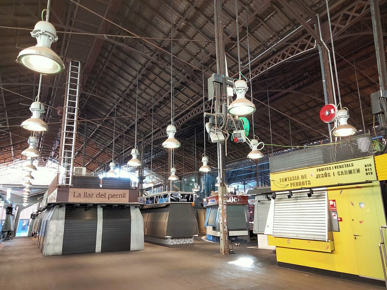 The empty hall of the Boqueria between stalls, with lamps hanging from the iron roof.