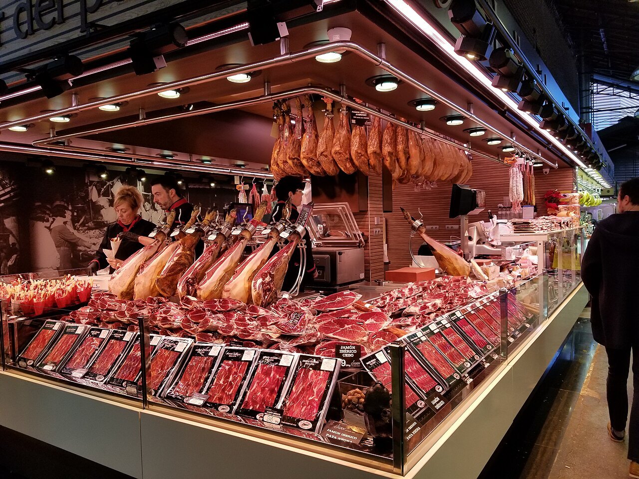 A butcher's stall in the Boqueria, with hams hanging above cuts of meat.