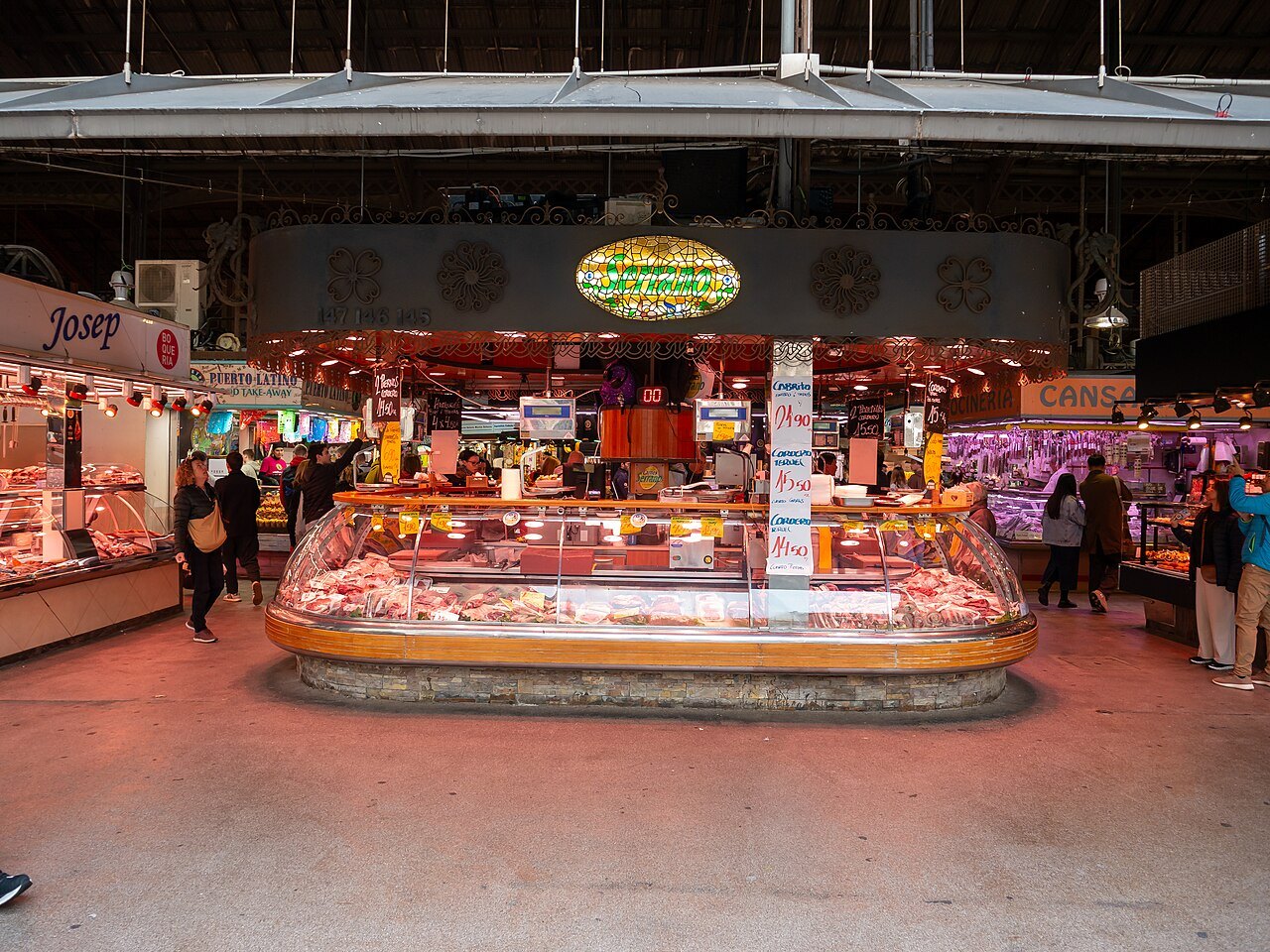 A central counter of fresh meat in the Boqueria hall, shoppers around it.