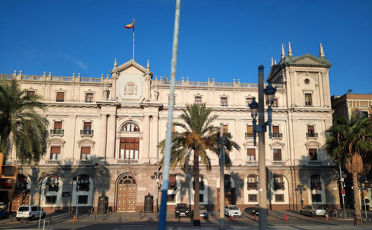 A grand stone building with palm trees in front of it on the Rambla.