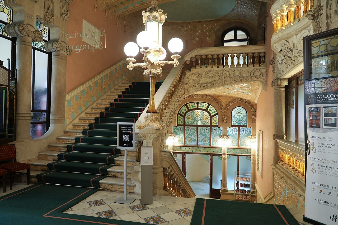 The staircase hall of the Palau de la Música, with a tall lamp and stained-glass windows.