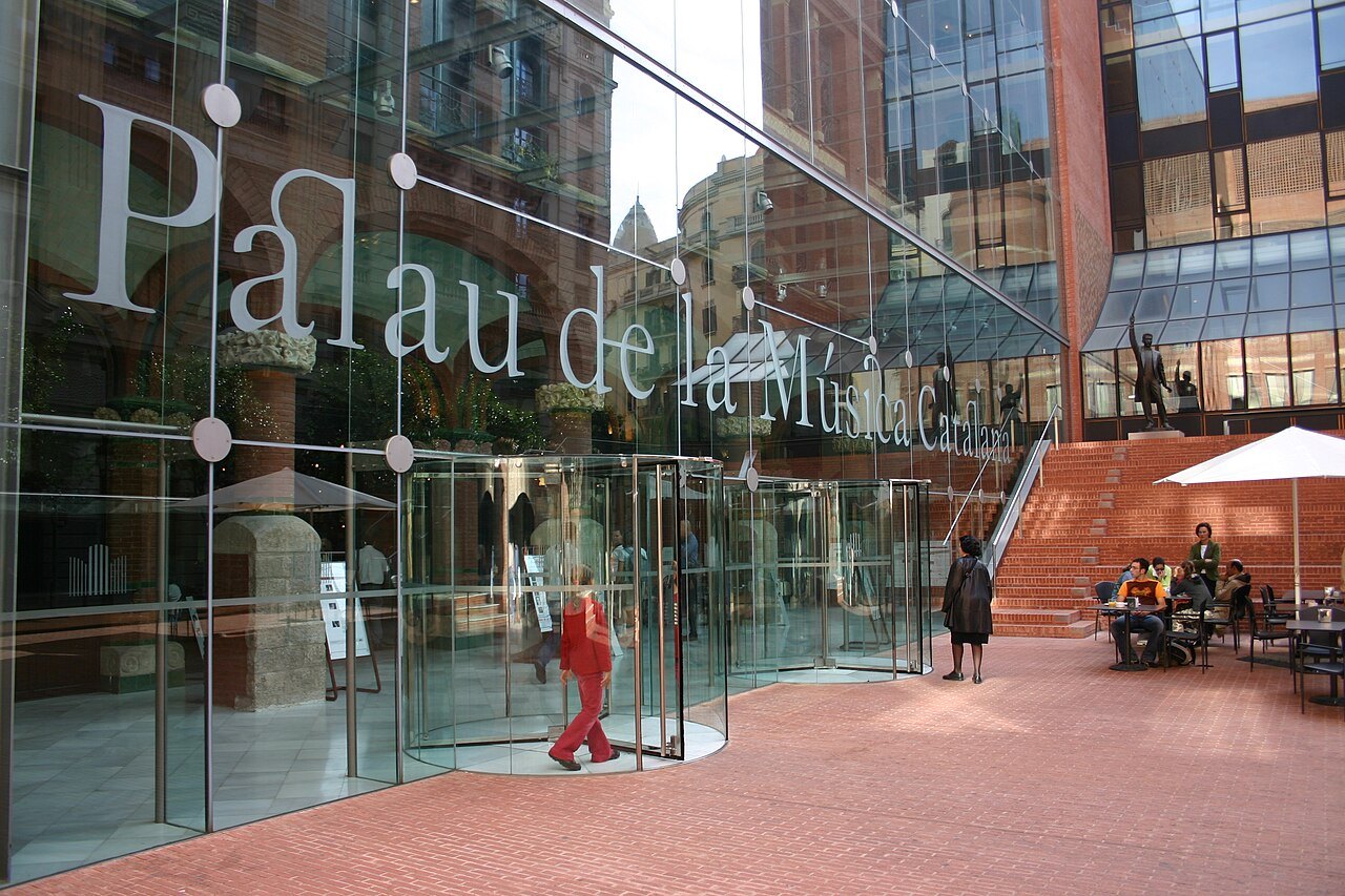 The glass entrance of the Palau de la Música, with its name in large letters over a red-brick plaza.