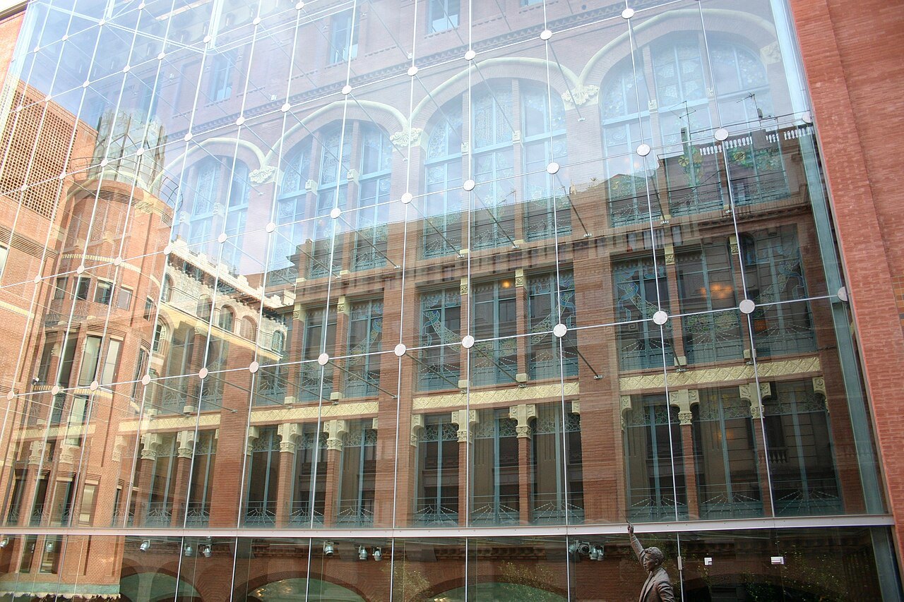 The glass wall of the Palau's modern wing, reflecting its brick and window frames.