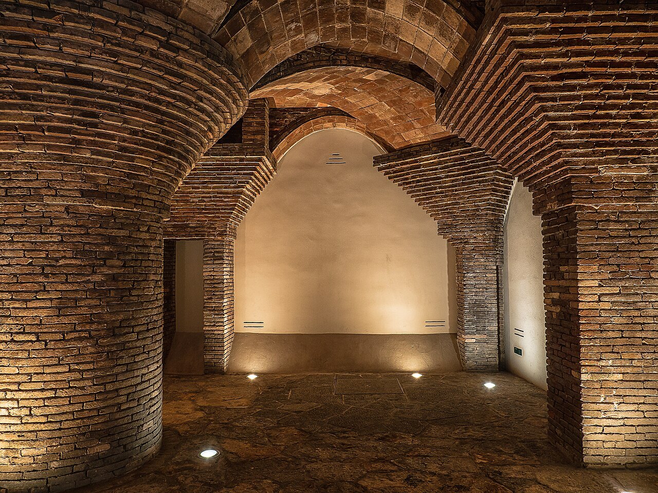 A brick-vaulted hall at the Palau Güell, lit from the floor.