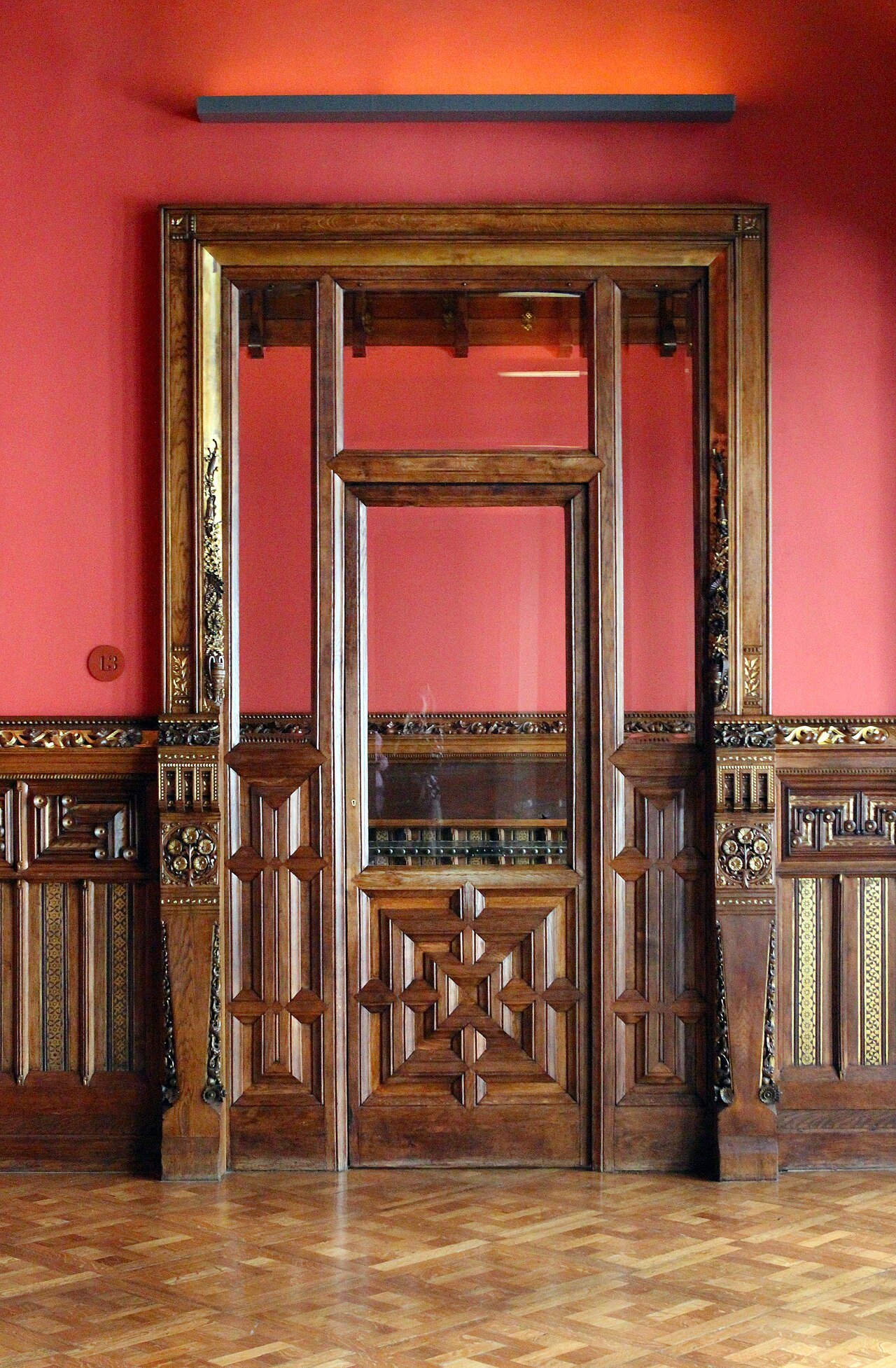A carved wooden door frame in a red-walled room of the Palau Güell.