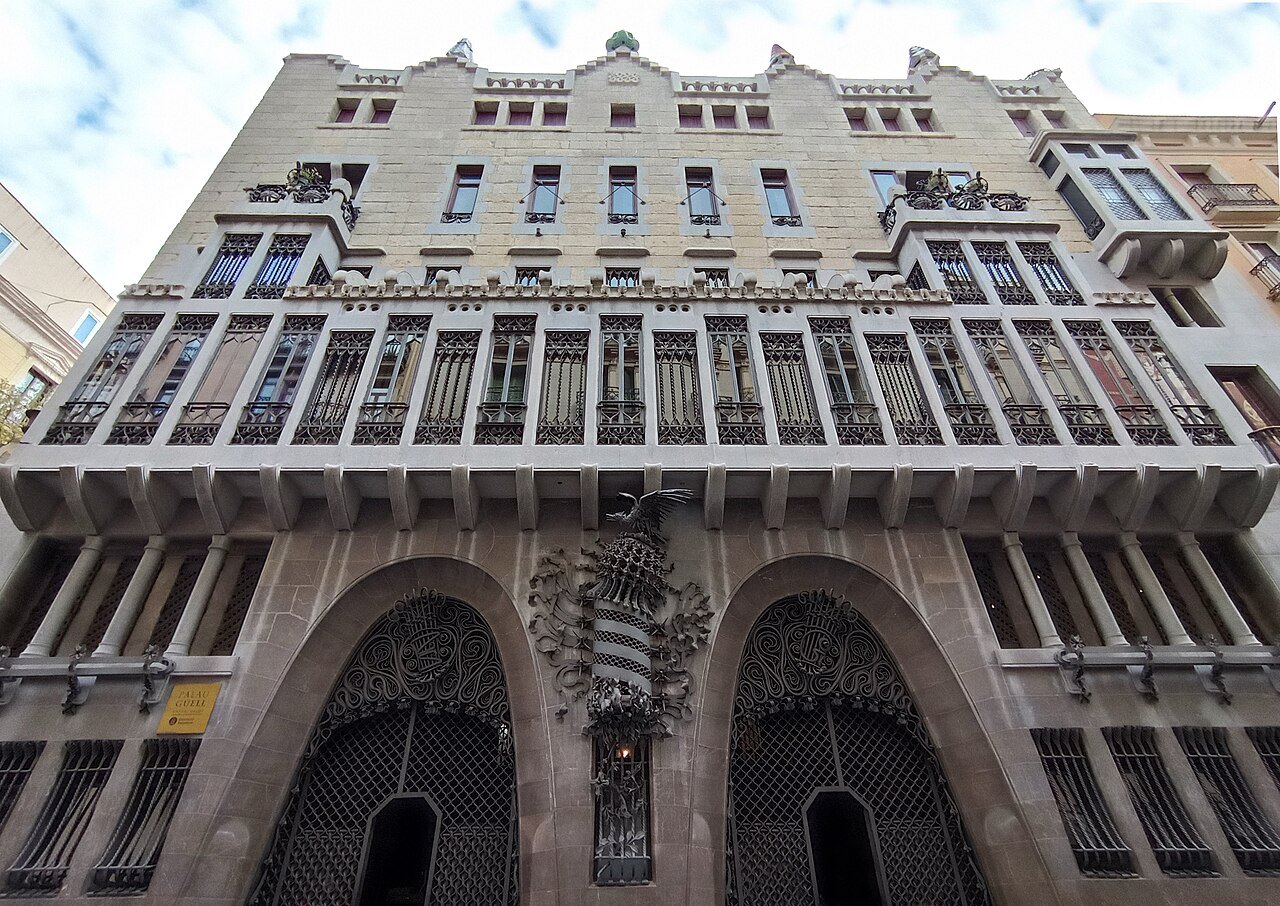 The façade of the Palau Güell seen from below, with arched doorways under a carved gallery.