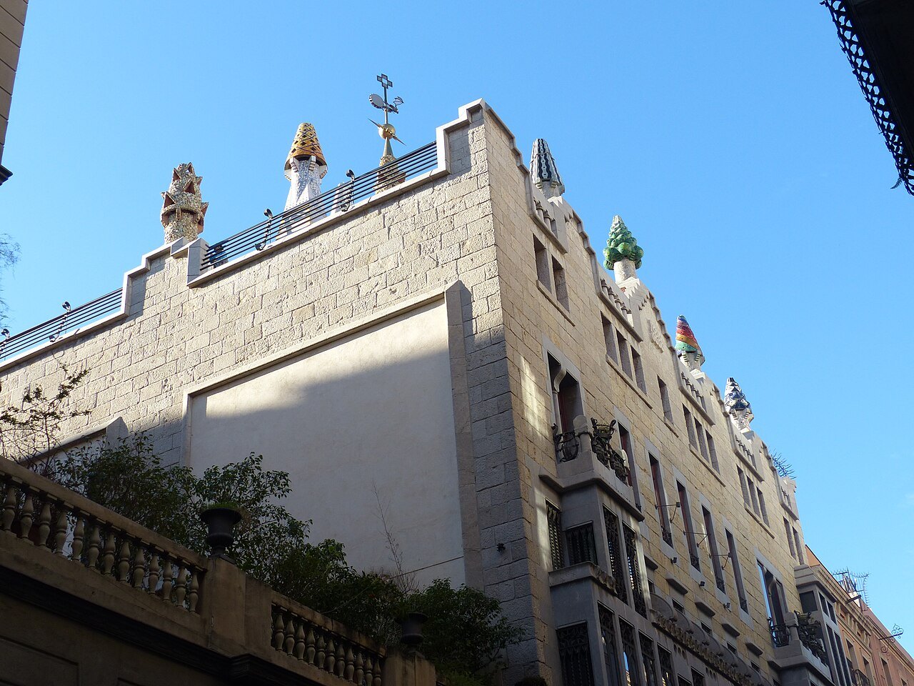 The stone corner of the Palau Güell, with chimneys on the roof against a blue sky.